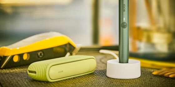 جهاز IQOS ILUMA على قاعدة شحن مع شاحن جيب على الطاولة.