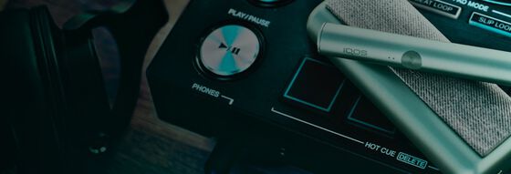 شاحن جيب وأنبوب تسخين IQOS ILUMA PRIME باللون الأخضر الزمردي على مشغل أسطوانات منسق أغاني (DJ).