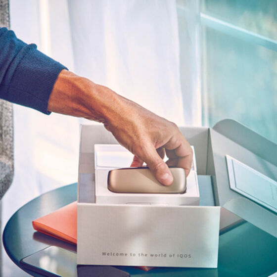 A gold IQOS device out of his packaging, accessories and a mobile on a table