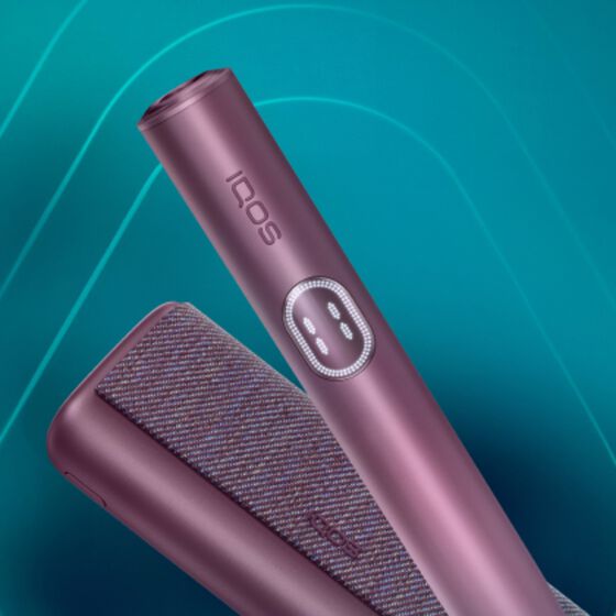 Close-up of IQOS ILUMA i Prime in a metallic plum color with its holder and case displayed against a teal background.