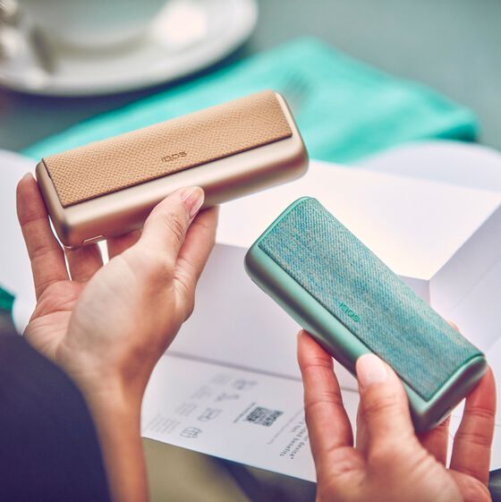 Two people comparing jade green and bronze taupe IQOS ILUMA PRIME devices..