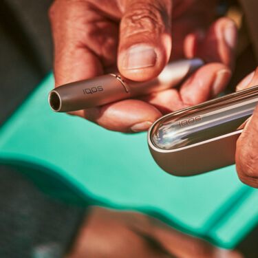 Brilliant gold IQOS 3 DUO with HEETS stick in hand and charger