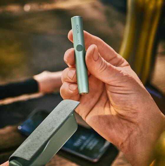 A moss green IQOS ILUMA Holder in a person's hand.