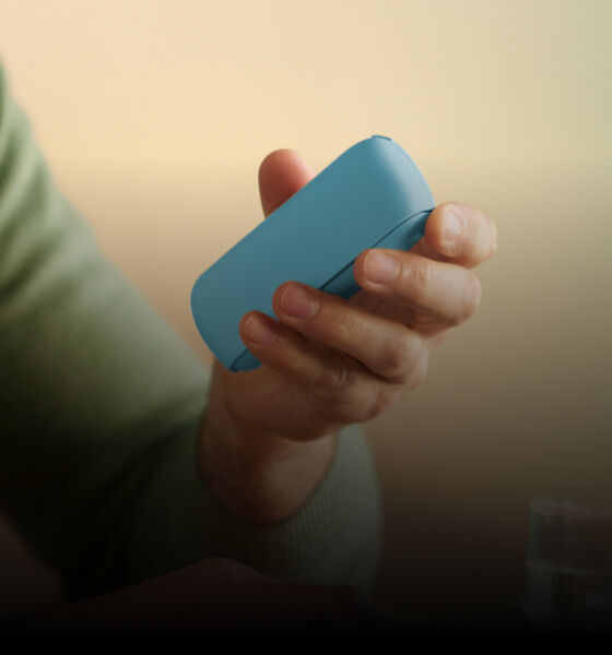 Man holding an IQOS Originals Duo pocket charger and typing on laptop