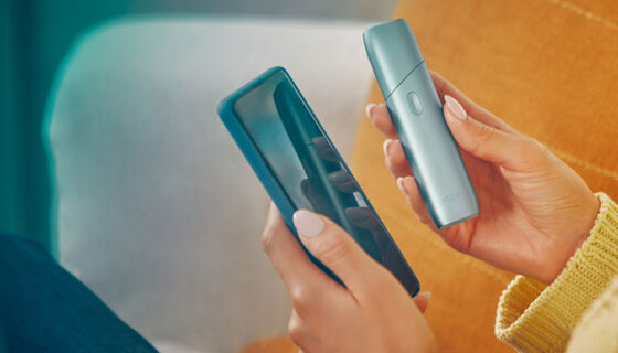Hands holding a mobile phone and IQOS Originals One device.