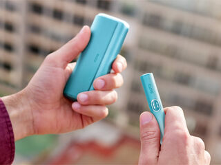 A woman holding an IQOS device looking at a laptop.