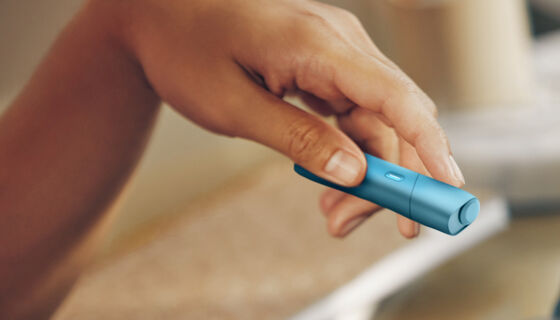 Hand holding turquoise IQOS Originals ONE heated tobacco device.