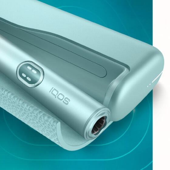 Close-up view of the IQOS ILUMA i PRIME device in an elegant mint-green finish, showcasing the holder and charger with a modern textured design.