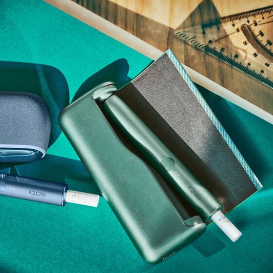 جهاز وشاحن IQOS ILUMA باللون الأخضر  موضوعان على مكتب.