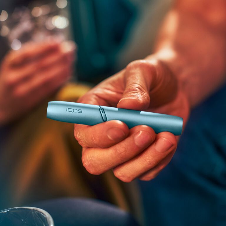 Hand holding IQOS Originals Duo holder in turquoise color.