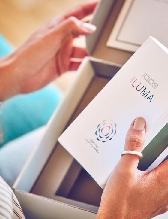 A person holding a box that contains a booklet on IQOS ILUMA.
