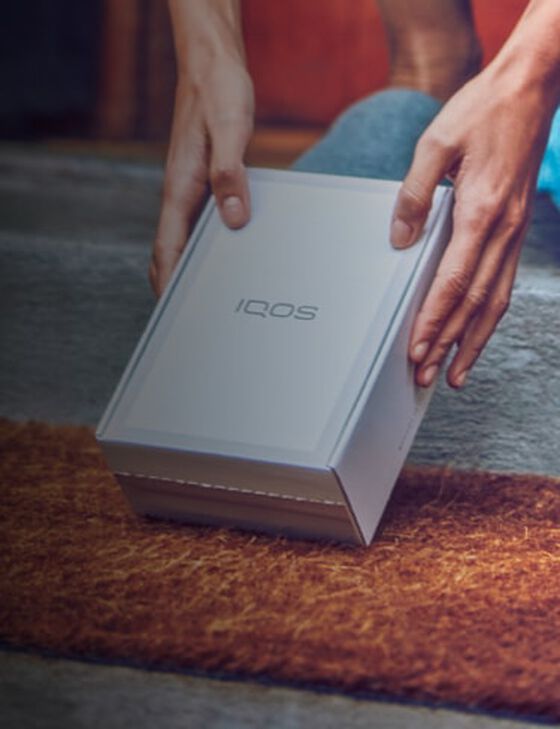Two hands picking up a IQOS device box.