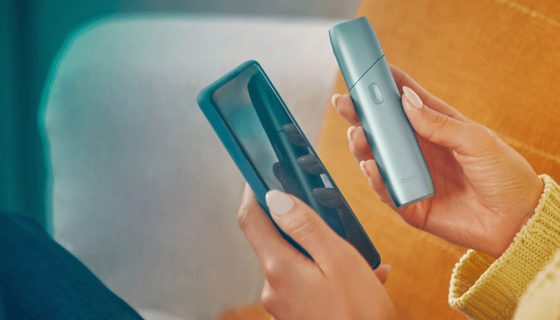يدان تمسكان هاتفاً محمولاً وجهاز IQOS Originals One.