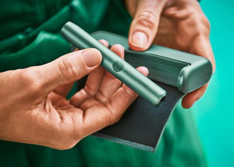 جهاز IQOS ILUMA PRIME باللون الأخضر  بيد مهندس معماري.