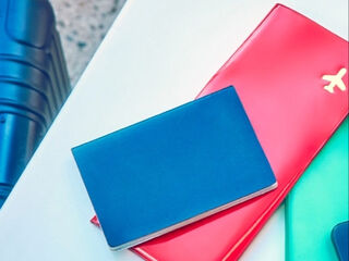A woman sitting at a table next to her suitcase with a smartphone, passport and plane ticket.