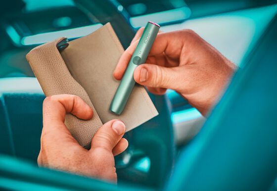 A person placing a jade green IQOS ILUMA PRIME Holder into a Pocket Charger covered with a full wrap.