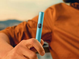 A woman holding an IQOS device looking at a laptop.