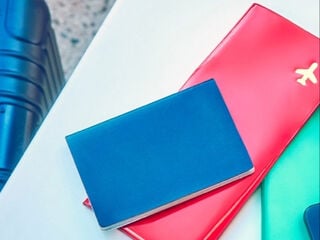 A woman sitting at a table next to her suitcase with a smartphone, passport and plane ticket.