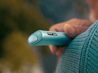 A hand holding a Pebble Beige IQOS ONE device.