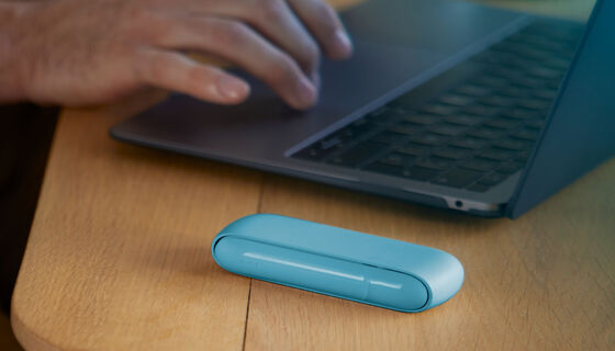 Hands typing on laptop and Iphone next to turquoise IQOS ORIGINALS DUO pocket charger.