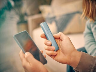 يدان تمسكان هاتفاً محمولاً وجهاز IQOS Originals One لتسجيل الدخول إلى myIqos، وذلك للاستفادة بأكبر قدر ممكن من جهاز التبغ المُسخَّن.