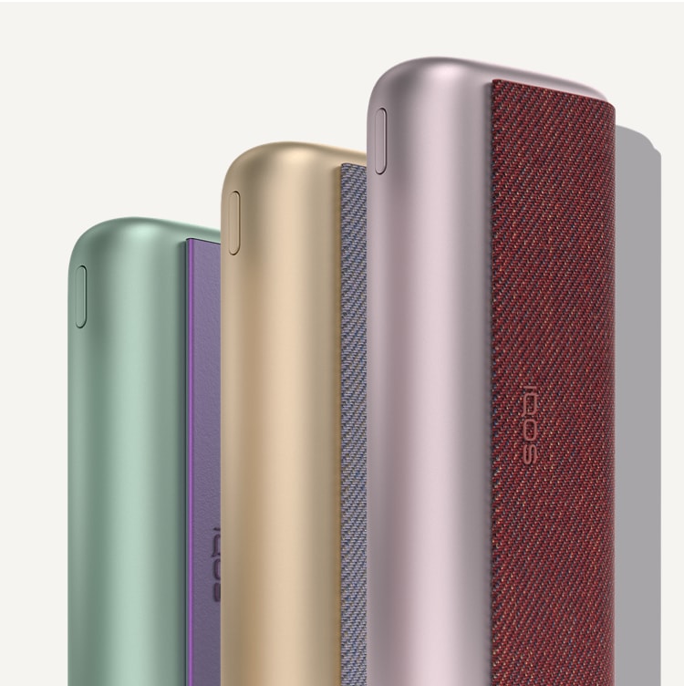 Three IQOS ILUMA PRIME devices: jade green, gold khaki and bronze taupe.